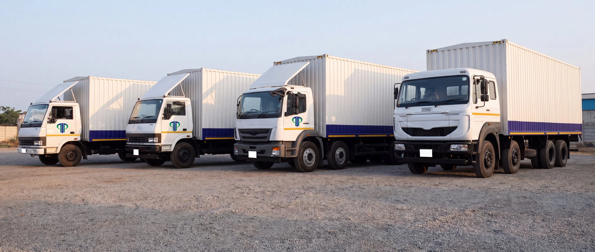 Four trucks in Patel Transport Agency livery, from a light truck to a heavy multi-axle, parked side by side in a yard